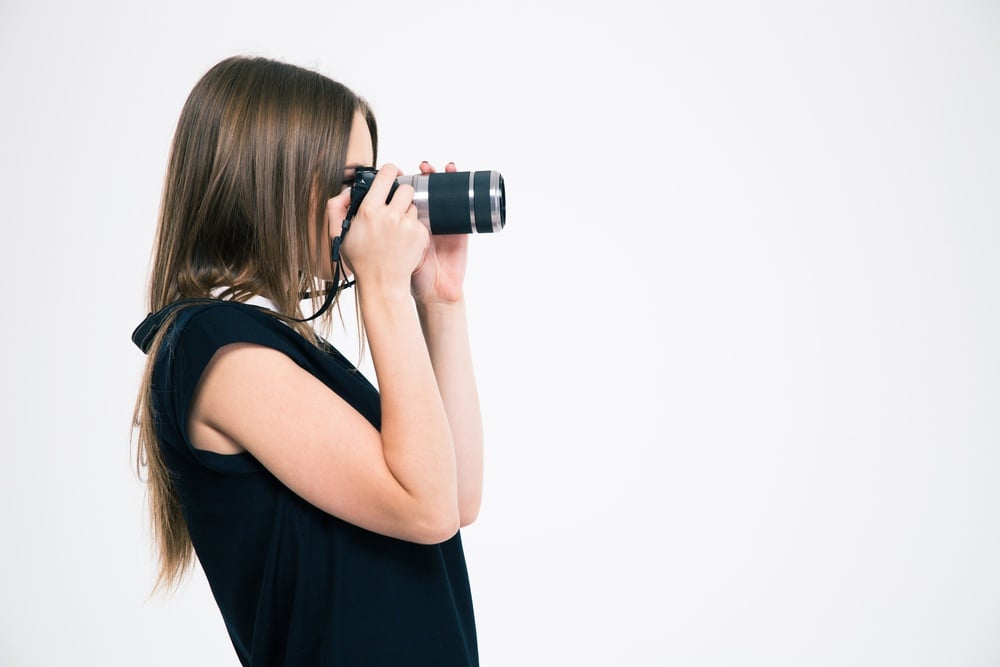 Side view portrait of a young woman making photo on camera isolated on a white background